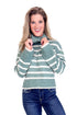 Woman wearing a green and white striped sweater with blue jeans on a white background