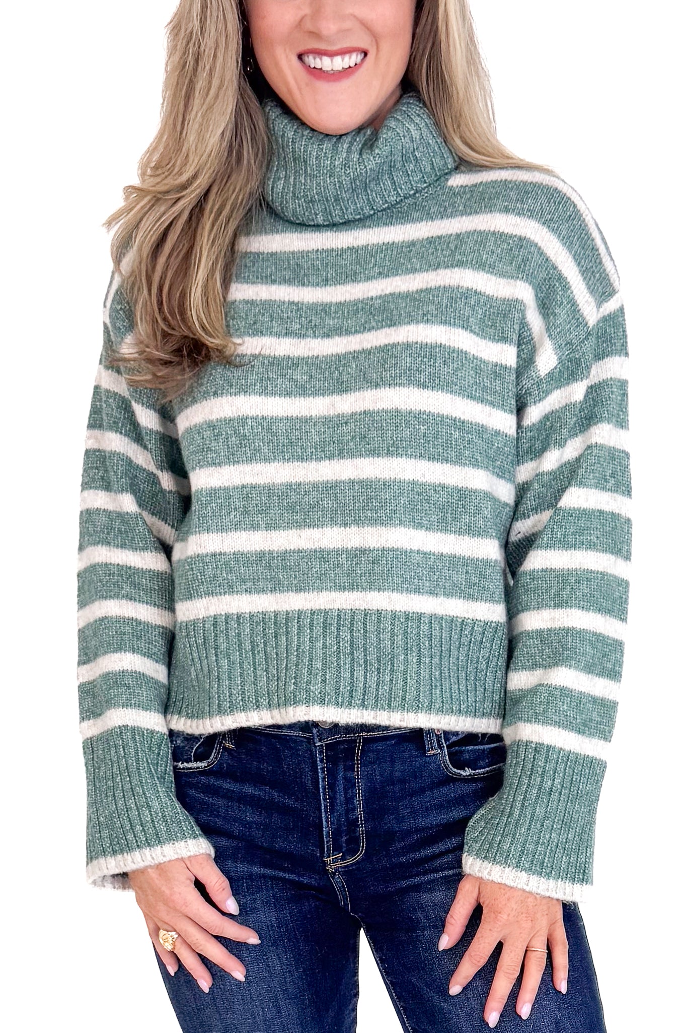 Woman wearing a green and white striped sweater with blue jeans on a plain background