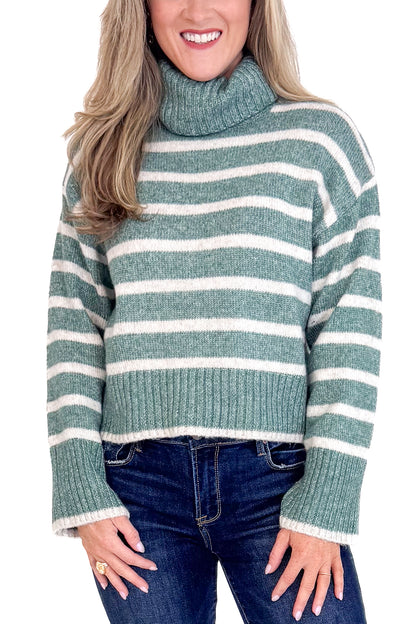 Woman wearing a green and white striped sweater with blue jeans on a plain background