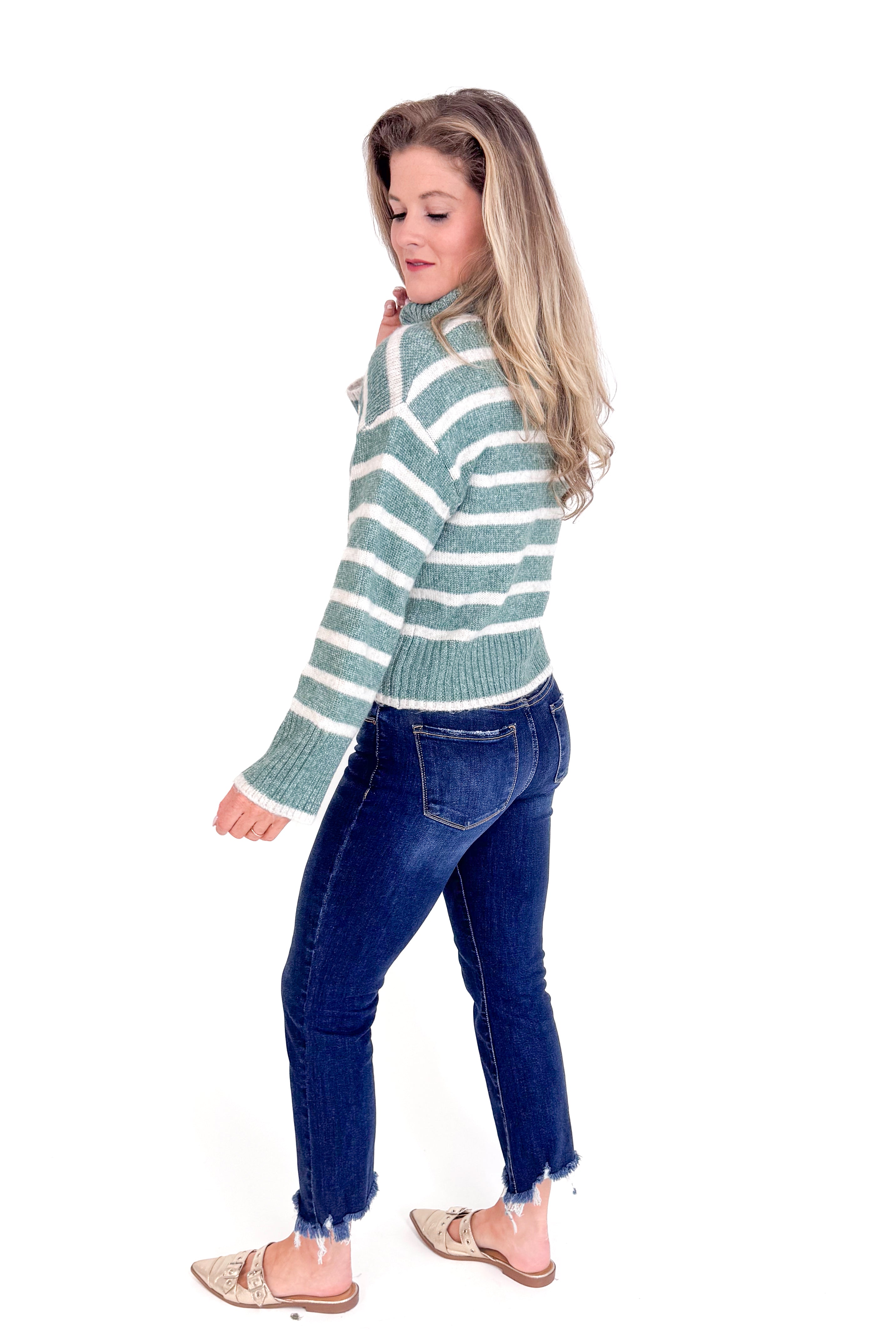 Woman wearing a green and white striped sweater and blue jeans on a white background