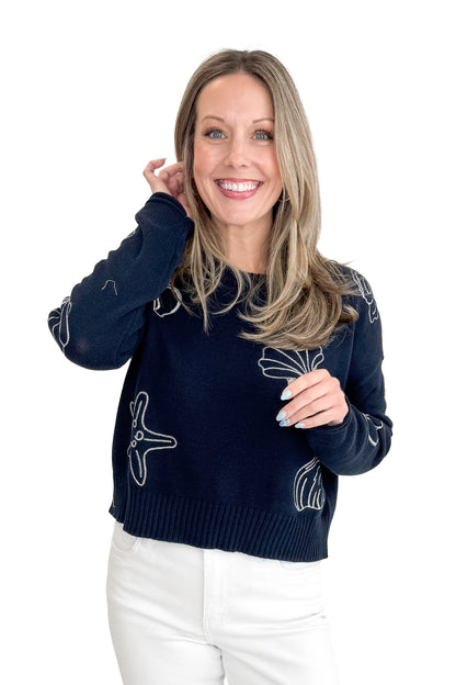 Front view of woman wearing True Navy Paradise Reef Sienna Sweater by Z Supply with jeans against white studio background.