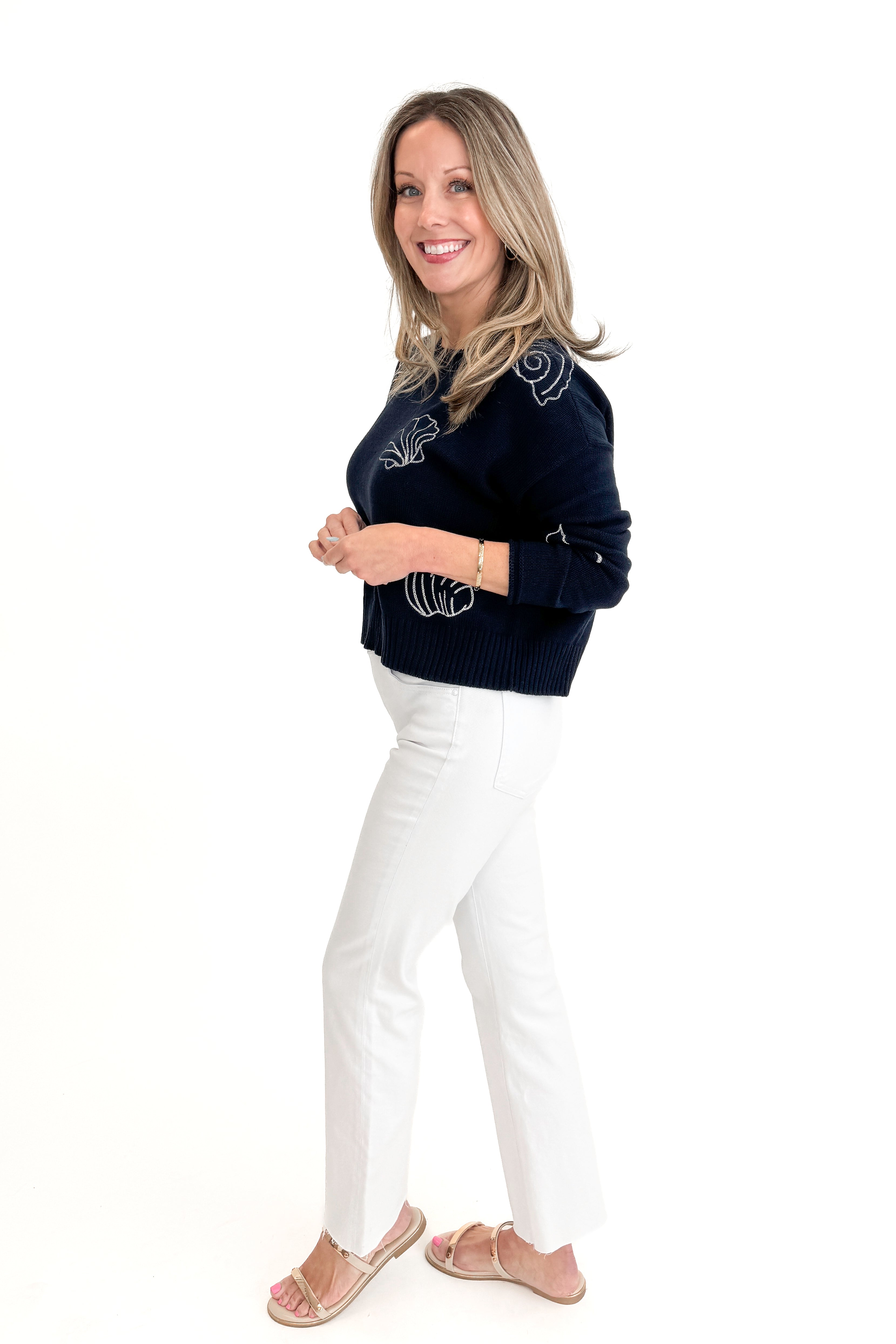 Side view of woman wearing True Navy Paradise Reef Sienna Sweater by Z Supply with jeans against white studio background.