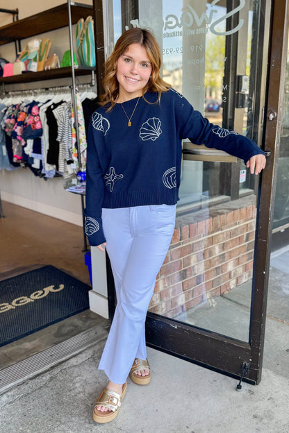 Front view of woman wearing True Navy Paradise Reef Sienna Sweater by Z Supply with jeans standing outside of Swagger Boutique.
