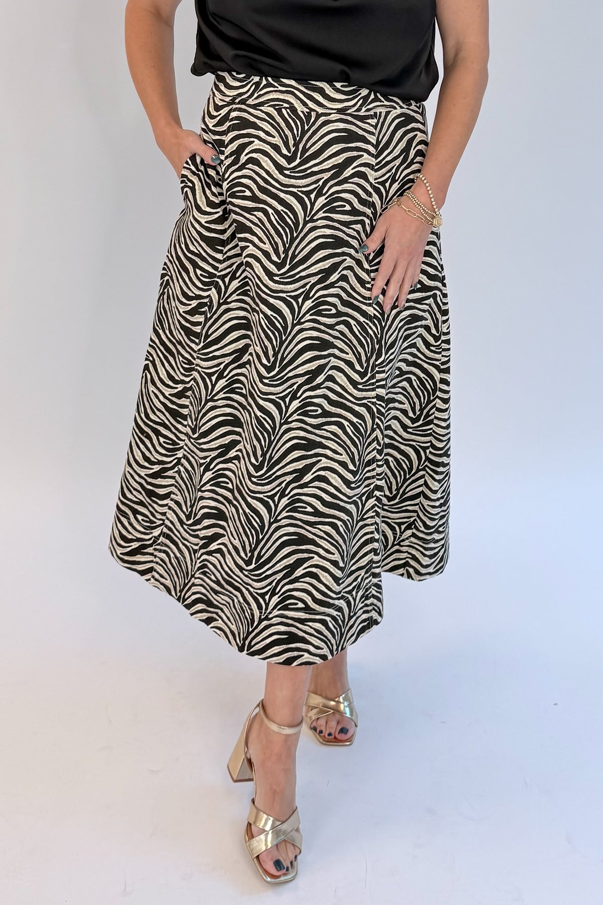 Front detail view of woman wearing Swagger Boutique’s Zebra Print Midi Skirt by Entro &amp; Black Satin Cowlneck Sleeveless Top  against white studio background.