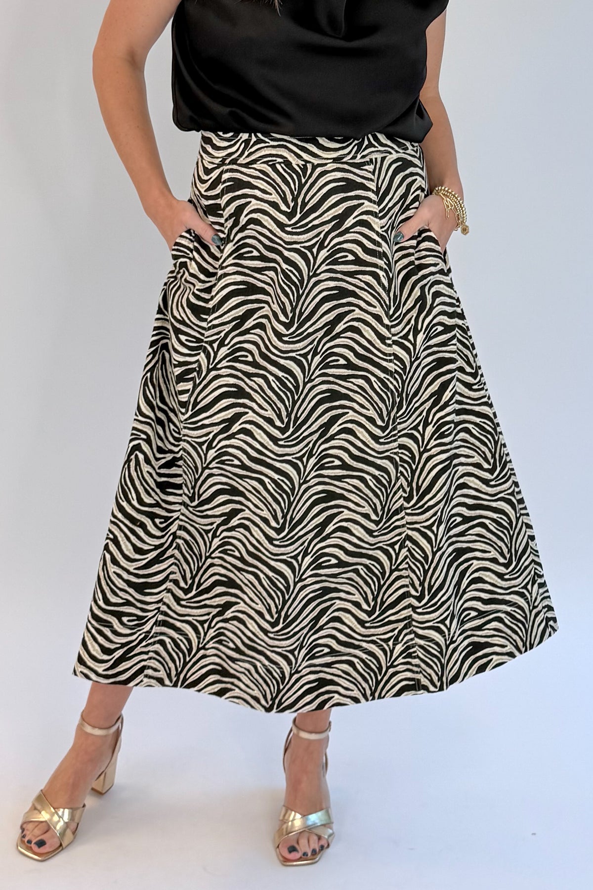 Front detail view of woman wearing Swagger Boutique’s Zebra Print Midi Skirt by Entro &amp; Black Satin Cowlneck Sleeveless Top  against white studio background.