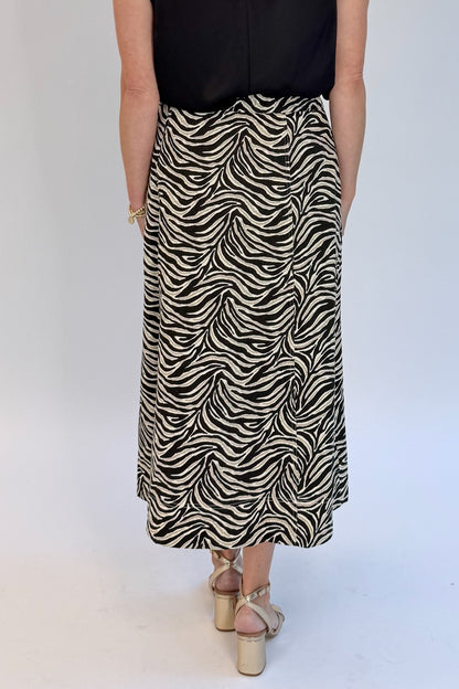 Back detail view of woman wearing Swagger Boutique’s Zebra Print Midi Skirt by Entro &amp; Black Satin Cowlneck Sleeveless Top  against white studio background.