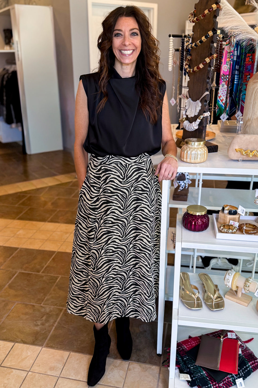 Front view of woman wearing Swagger Boutique’s Zebra Print Midi Skirt by Entro &amp; Black Satin Cowlneck Sleeveless Top  standing at the store.