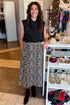 Front view of woman wearing Swagger Boutique’s Zebra Print Midi Skirt by Entro & Black Satin Cowlneck Sleeveless Top  standing at the store.