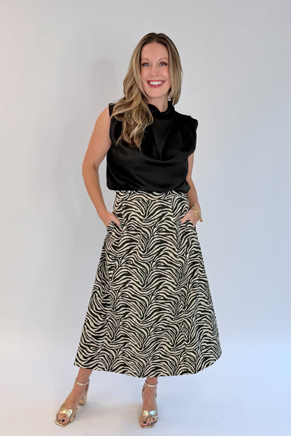 Front view of woman wearing Swagger Boutique’s Zebra Print Midi Skirt by Entro &amp; Black Satin Cowlneck Sleeveless Top  against white studio background.