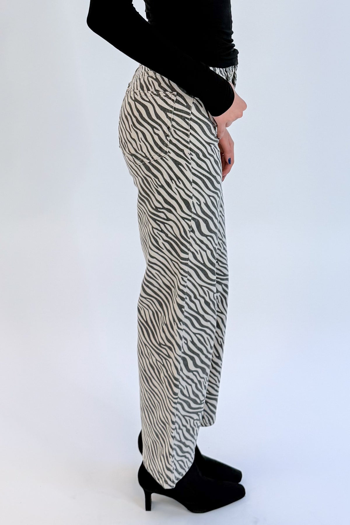 Side detail view of woman wearing Swagger Boutique’s top with Zebra Straight Leg Jeans by Just Black Denim against white studio background.