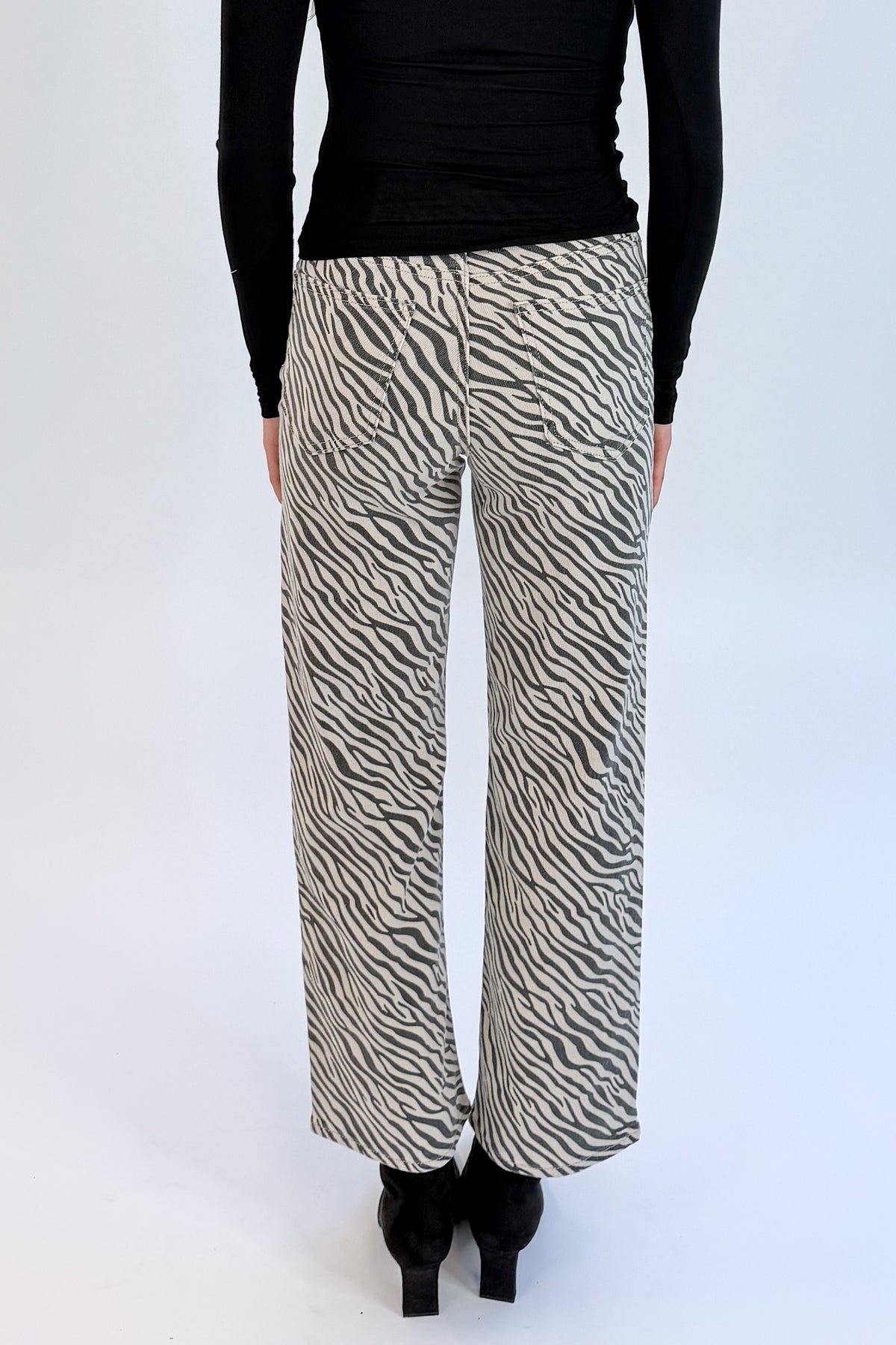 Back detail view of woman wearing Swagger Boutique’s top with Zebra Straight Leg Jeans by Just Black Denim against white studio background.