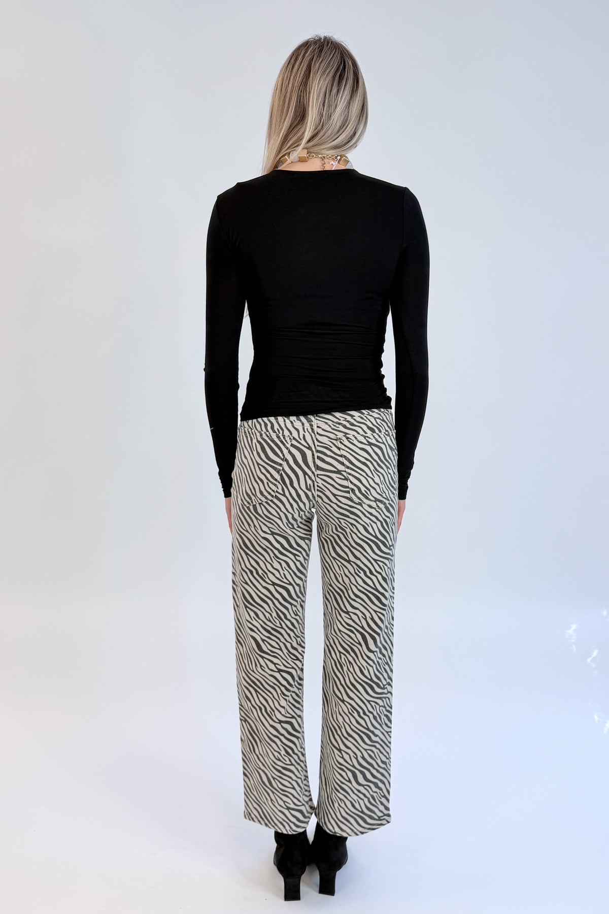 Back view of woman wearing Swagger Boutique’s top with Zebra Straight Leg Jeans by Just Black Denim against white studio background.