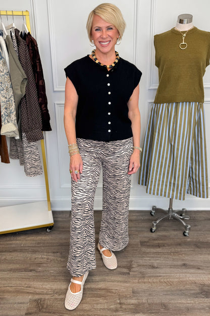 Front view of woman wearing Swagger Boutique’s Zebra Print Suede Pants with Black Sweater with clothing hanging in the background.