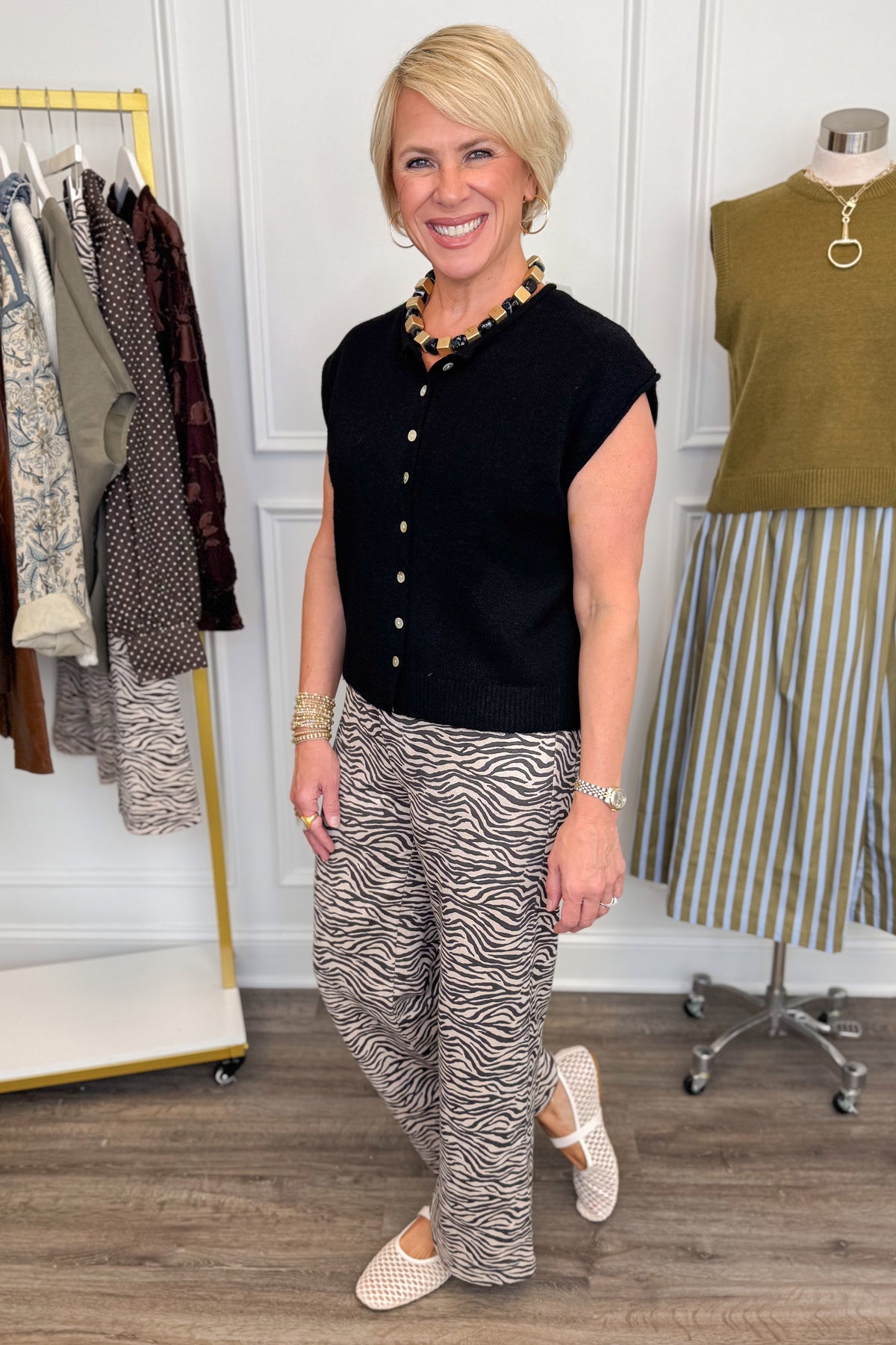 Side view of woman wearing Swagger Boutique’s Zebra Print Suede Pants with Black Sweater with clothing hanging in the background.