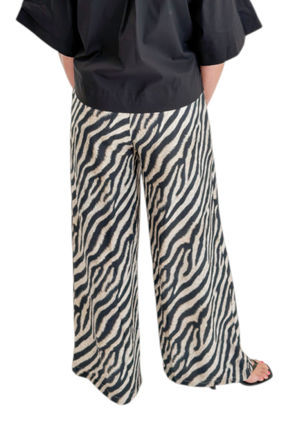 Back view of woman wearing Swagger Boutique’s Black Collared Short Sleeve Top with Zebra Wide Leg Pants by Entro against white studio background.