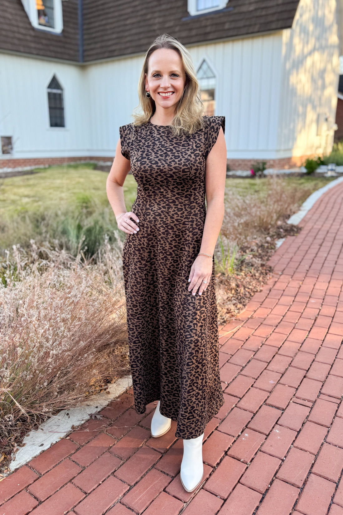 Woman in a leopard print dress standing on a brick path with a house in the background