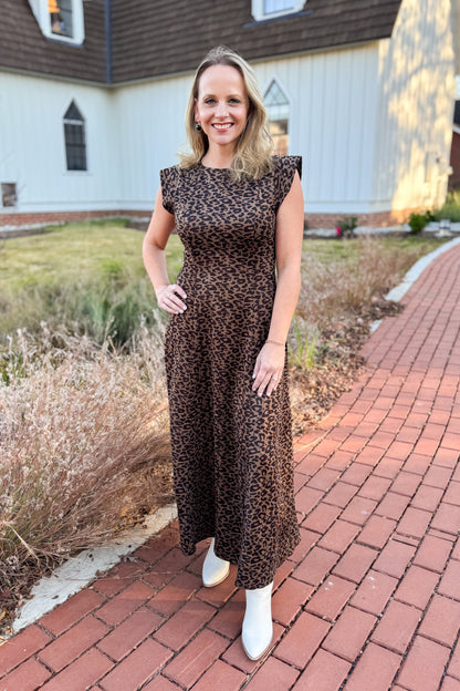 Woman in a leopard print dress standing on a brick path with a house in the background