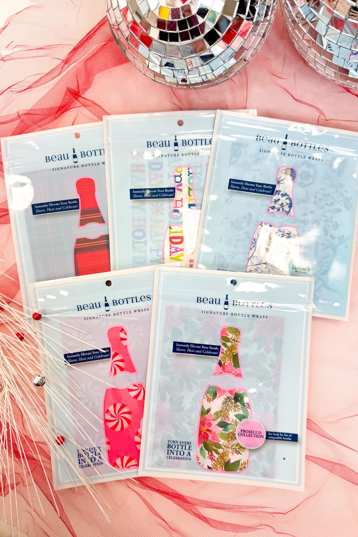 Set of beau bottle wraps in packaging on a pink fabric background with disco balls.