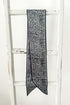 A long narrow scarf with a black and white leopard print pattern, draped over the rung of a white wooden ladder.