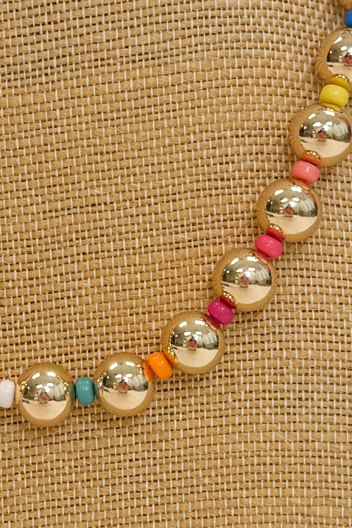 closeup of a gold and colorful beaded necklace on a burlap necklace stand 