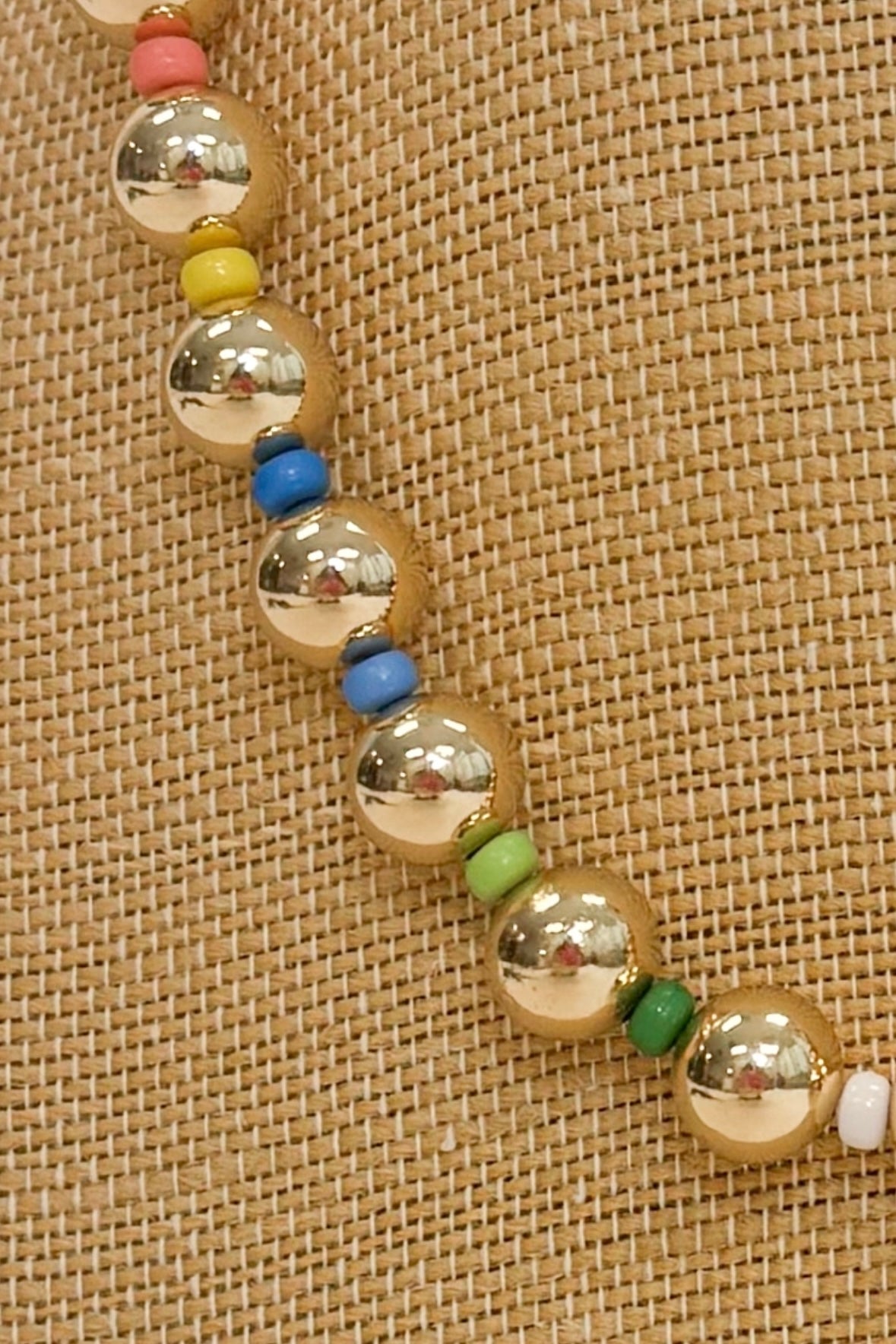 closeup of a gold and colorful beaded necklace on a burlap necklace stand 