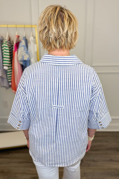 Person wearing a blue and white striped shirt in a room with clothes on a rack.