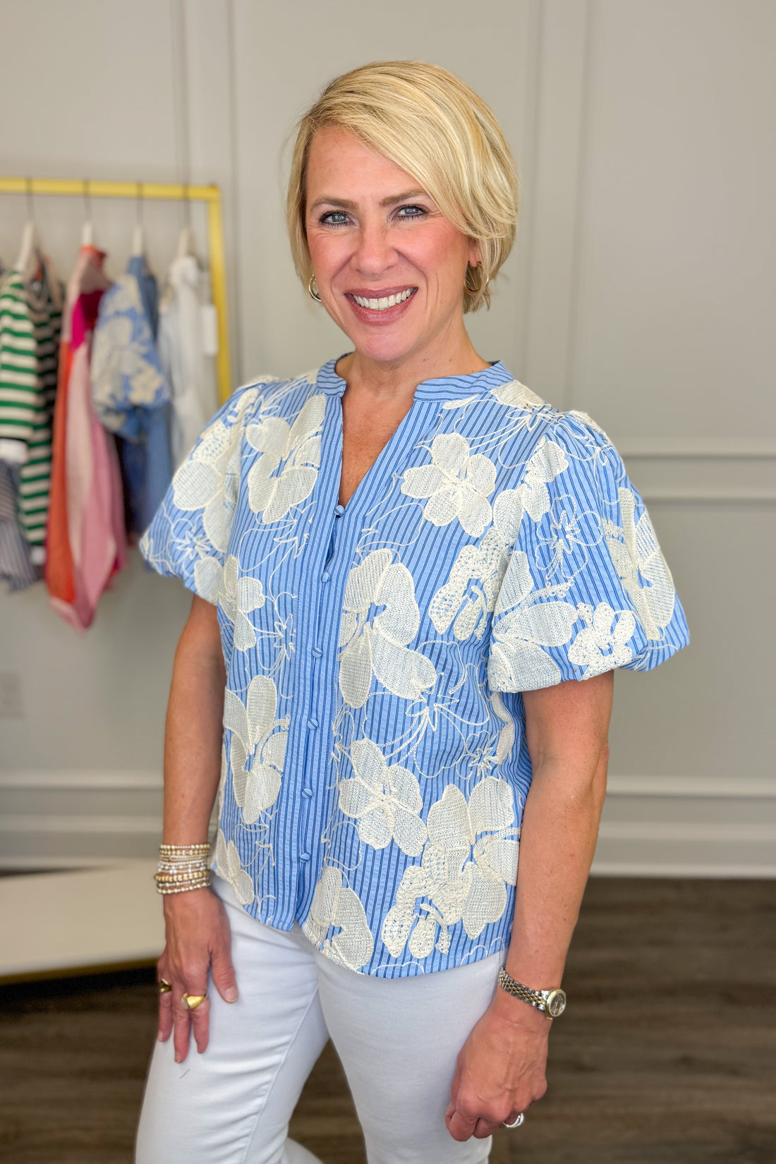Woman wearing a blue floral blouse in a room with clothes on a rack.