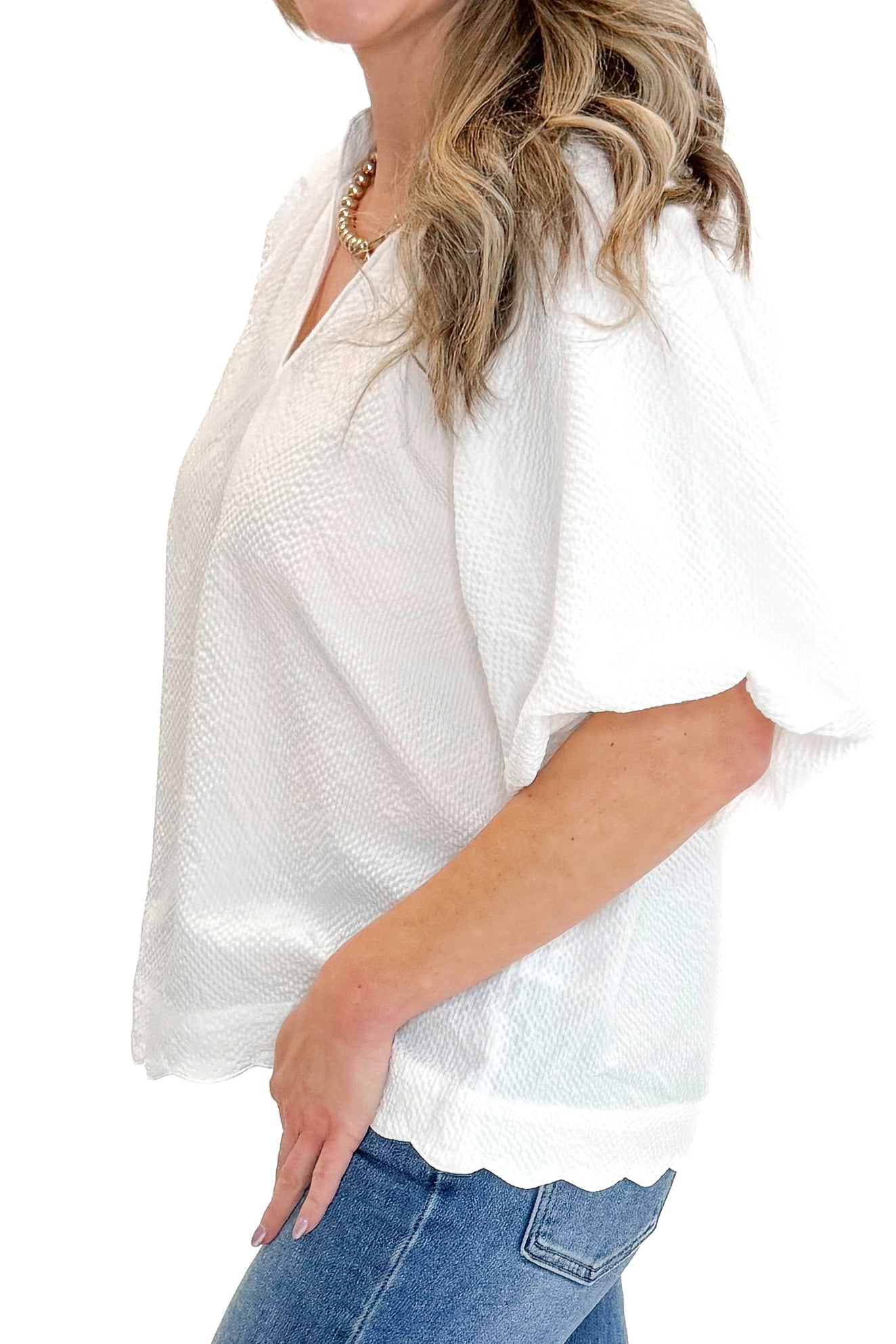 Side view of woman wearing White Scallop Detail V-neck Top with jeans against white studio background.