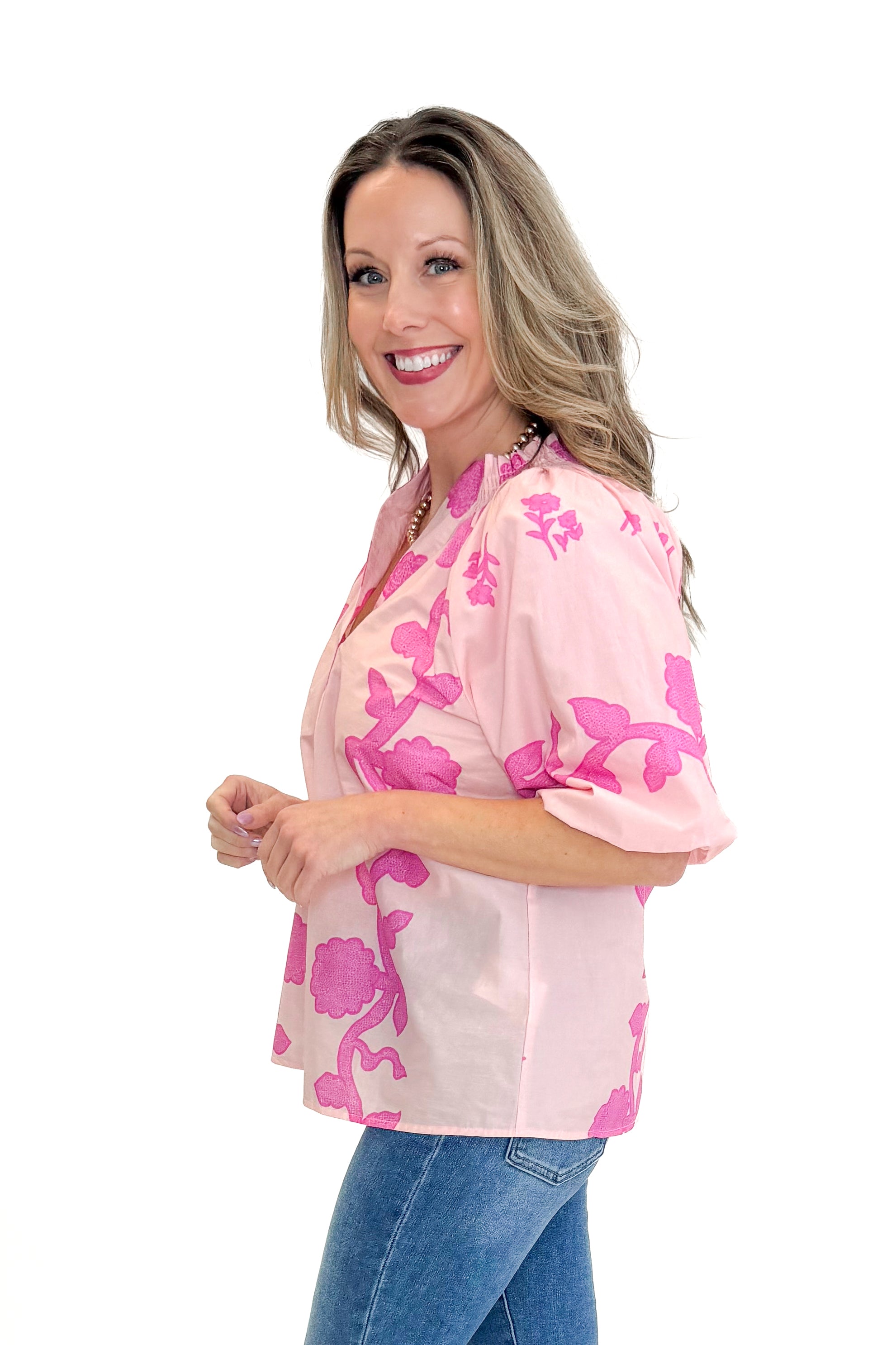Side view of woman wearing Pink Floral Lace Print Top with jeans against white studio background.