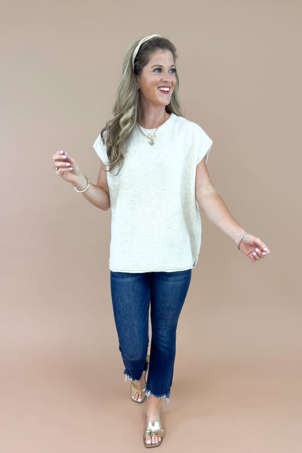 Woman wearing a white top and blue jeans on a beige background
