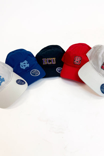 Five baseball caps in different colors arranged in a semi-circle on a white background: white with a light blue UNC logo, blue with a white NC logo, black with gold and white ECU lettering, red with gold and white SC lettering, and white with red and gold SC lettering.