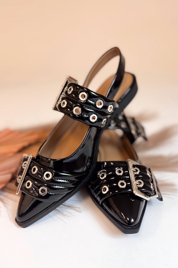 Black patent leather shoes with decorative straps on a light background