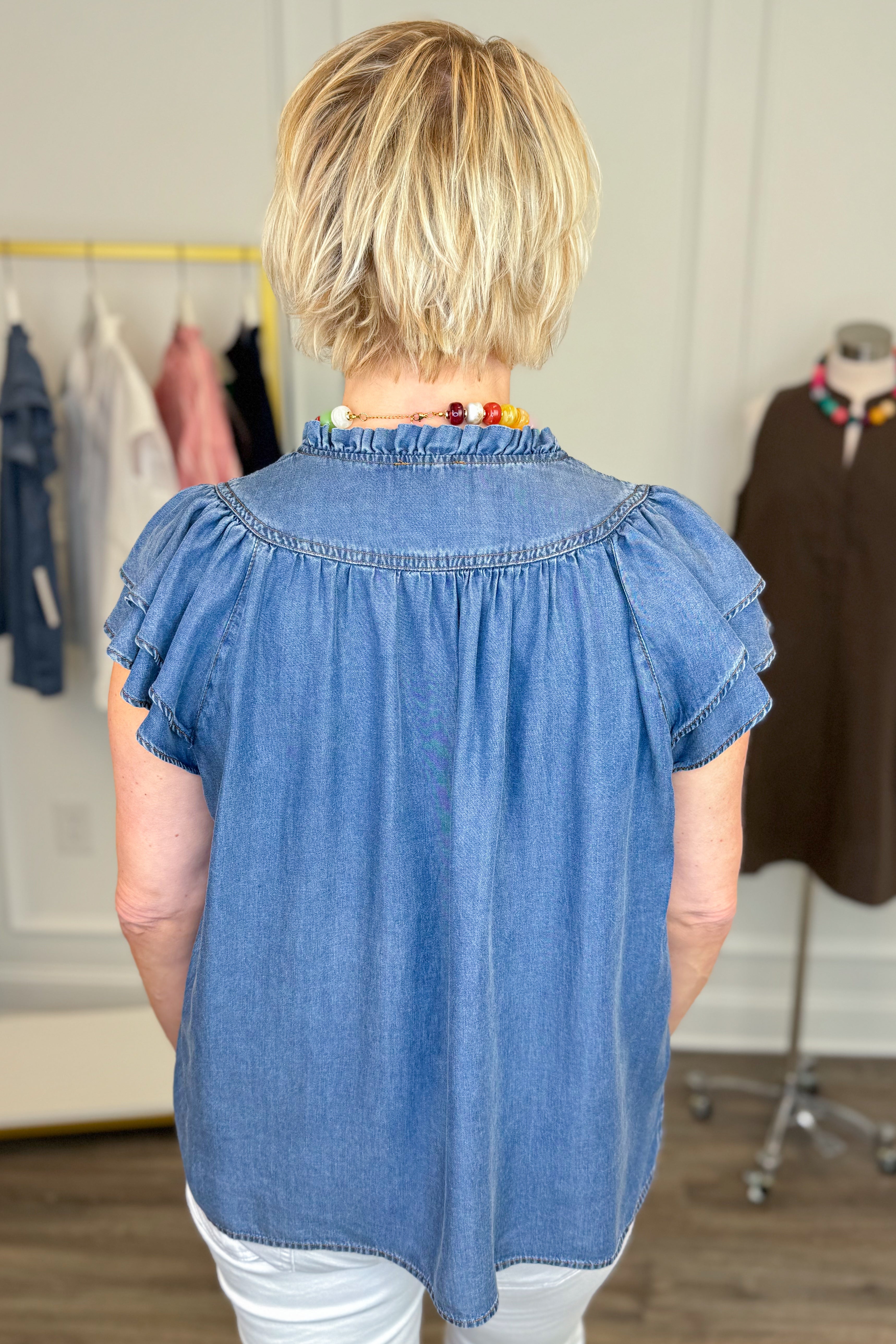 Person wearing a blue denim top with ruffled sleeves in a clothing store.