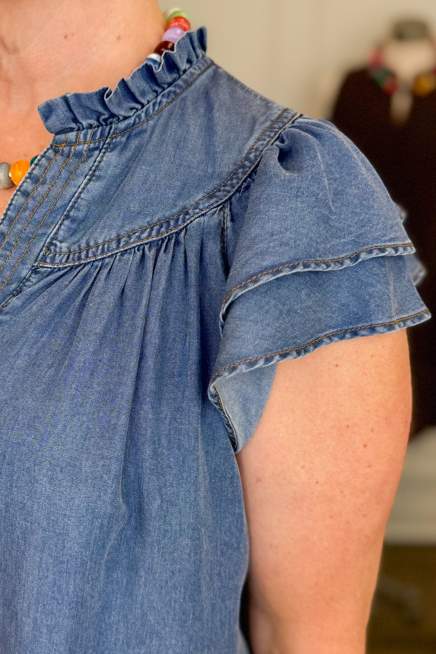 Close-up of a person wearing a blue denim shirt with ruffled shoulders.