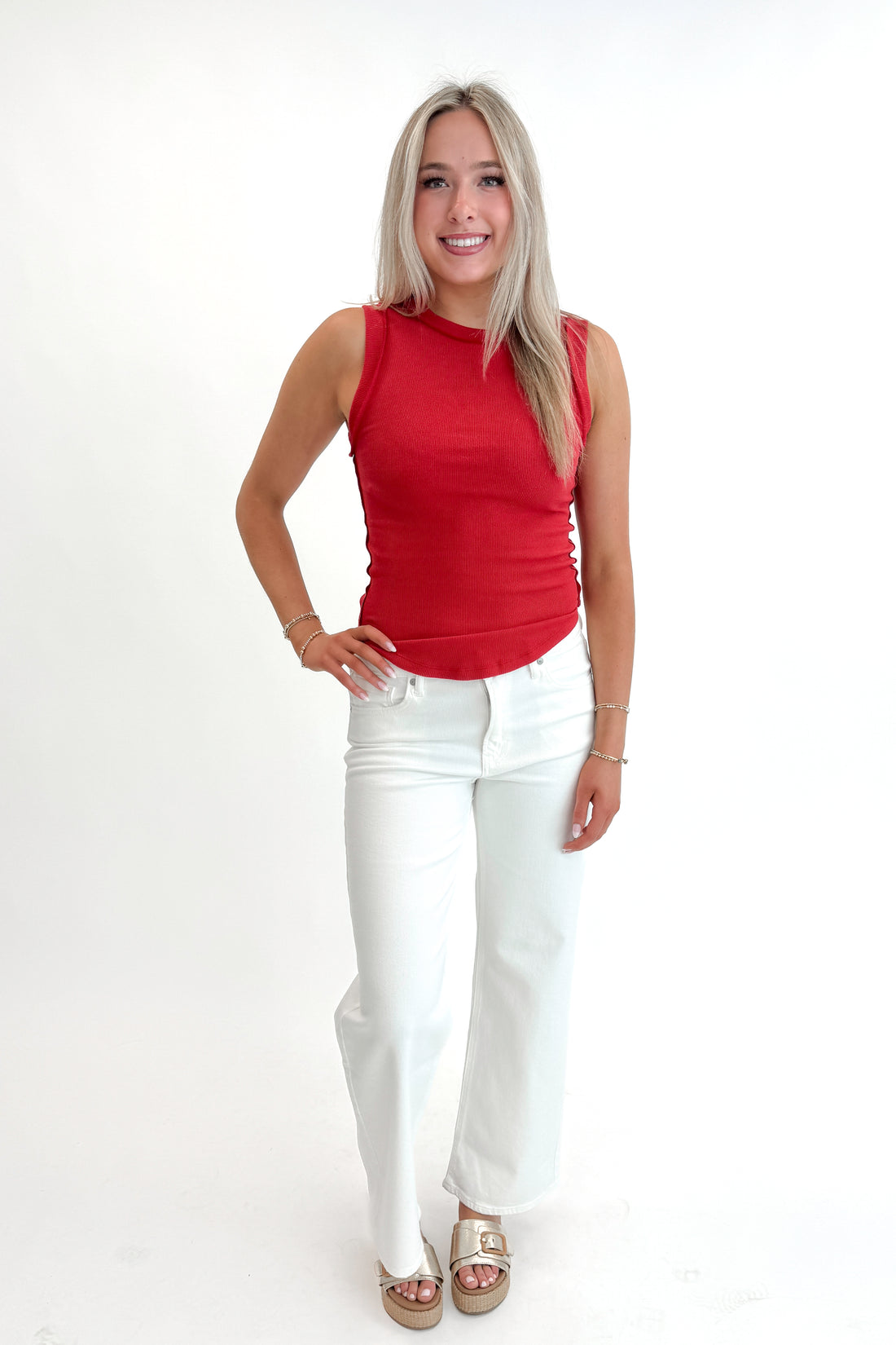 Front view of woman wearing Red Round Hem Ribbed Tank with jeans against white studio background.