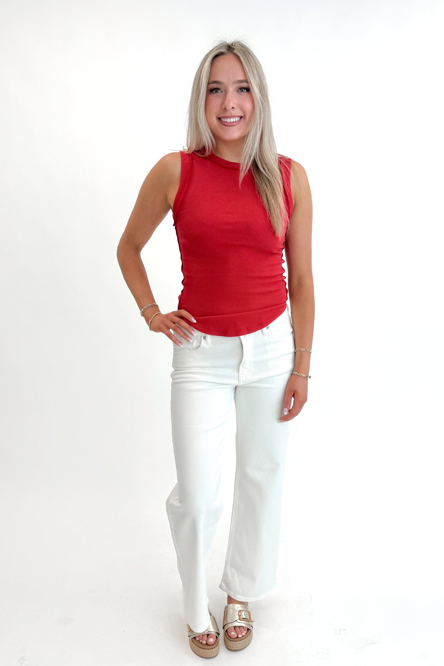 Front view of woman wearing Red Round Hem Ribbed Tank with jeans against white studio background.