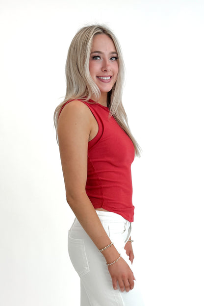 Side view of woman wearing Red Round Hem Ribbed Tank with jeans against white studio background.