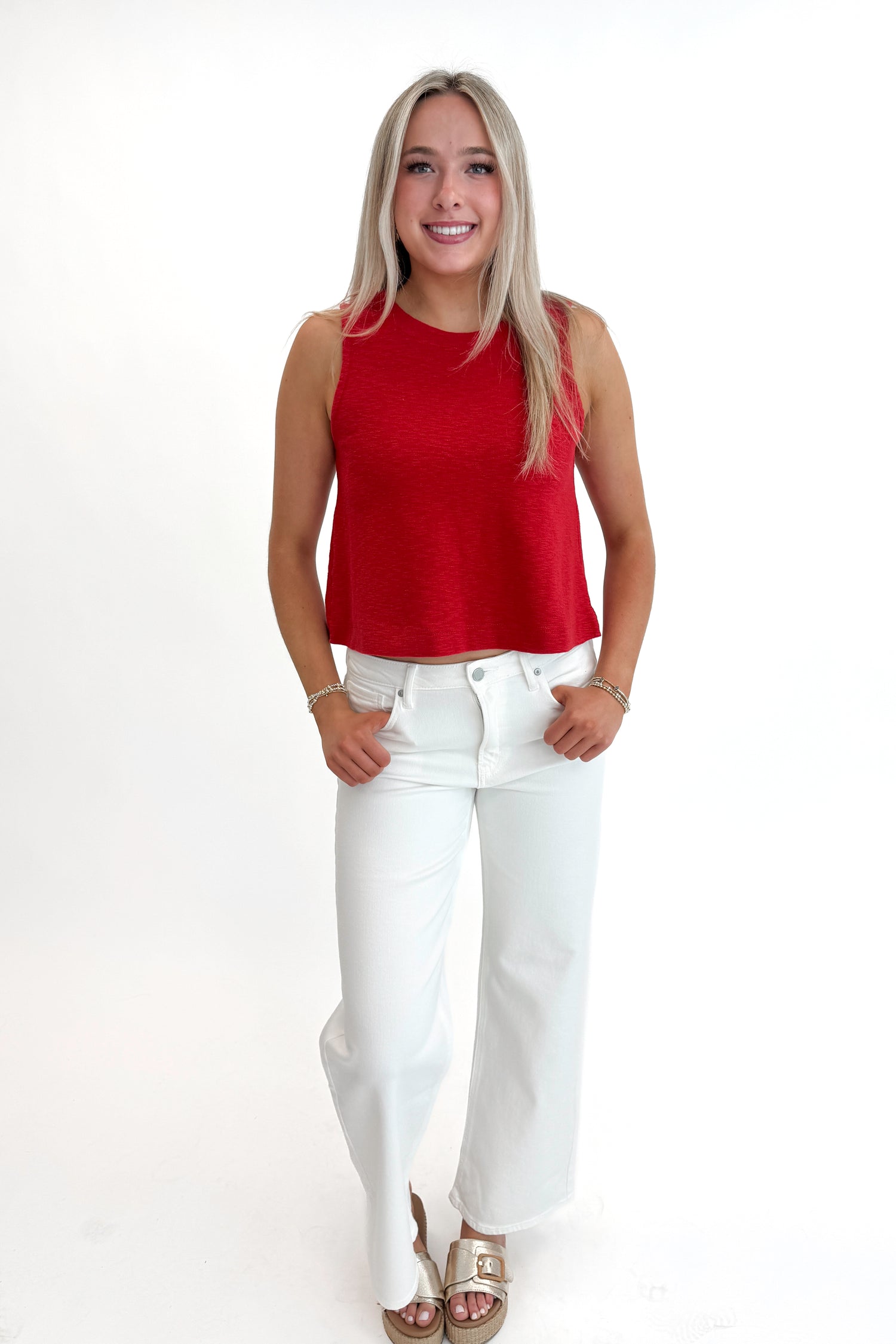 Front view of woman wearing Red Boxy Tank Top with white jeans against white studio background.
