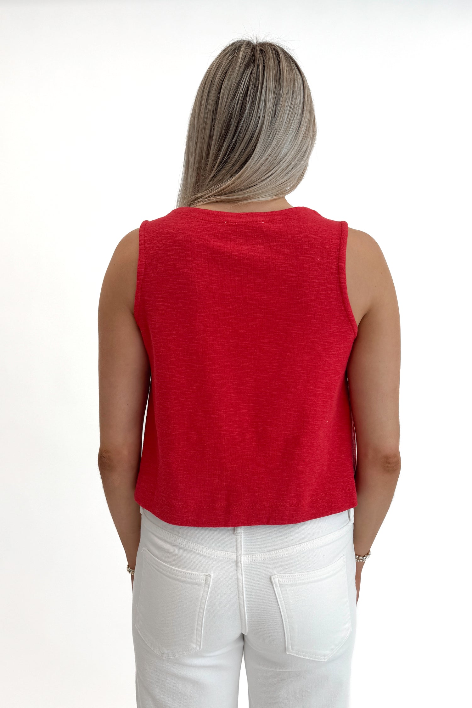 Back view of woman wearing Red Boxy Tank Top with white jeans against white studio background.