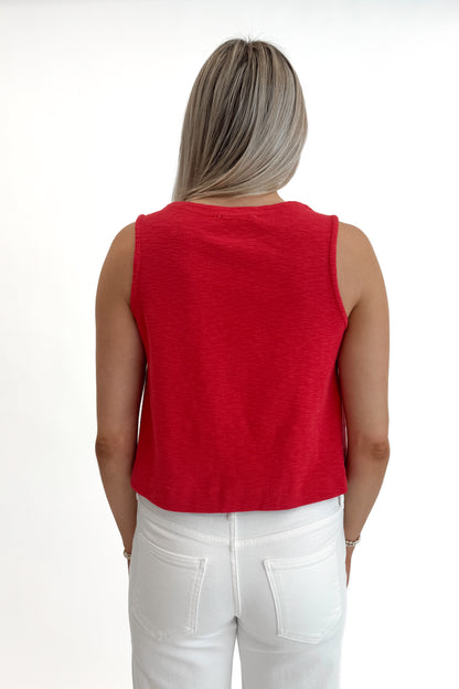 Back view of woman wearing Red Boxy Tank Top with white jeans against white studio background.