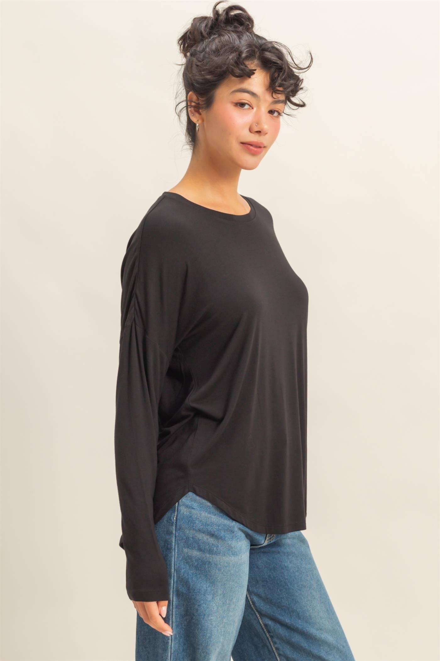 Woman wearing a black long-sleeve top and blue jeans on a beige background