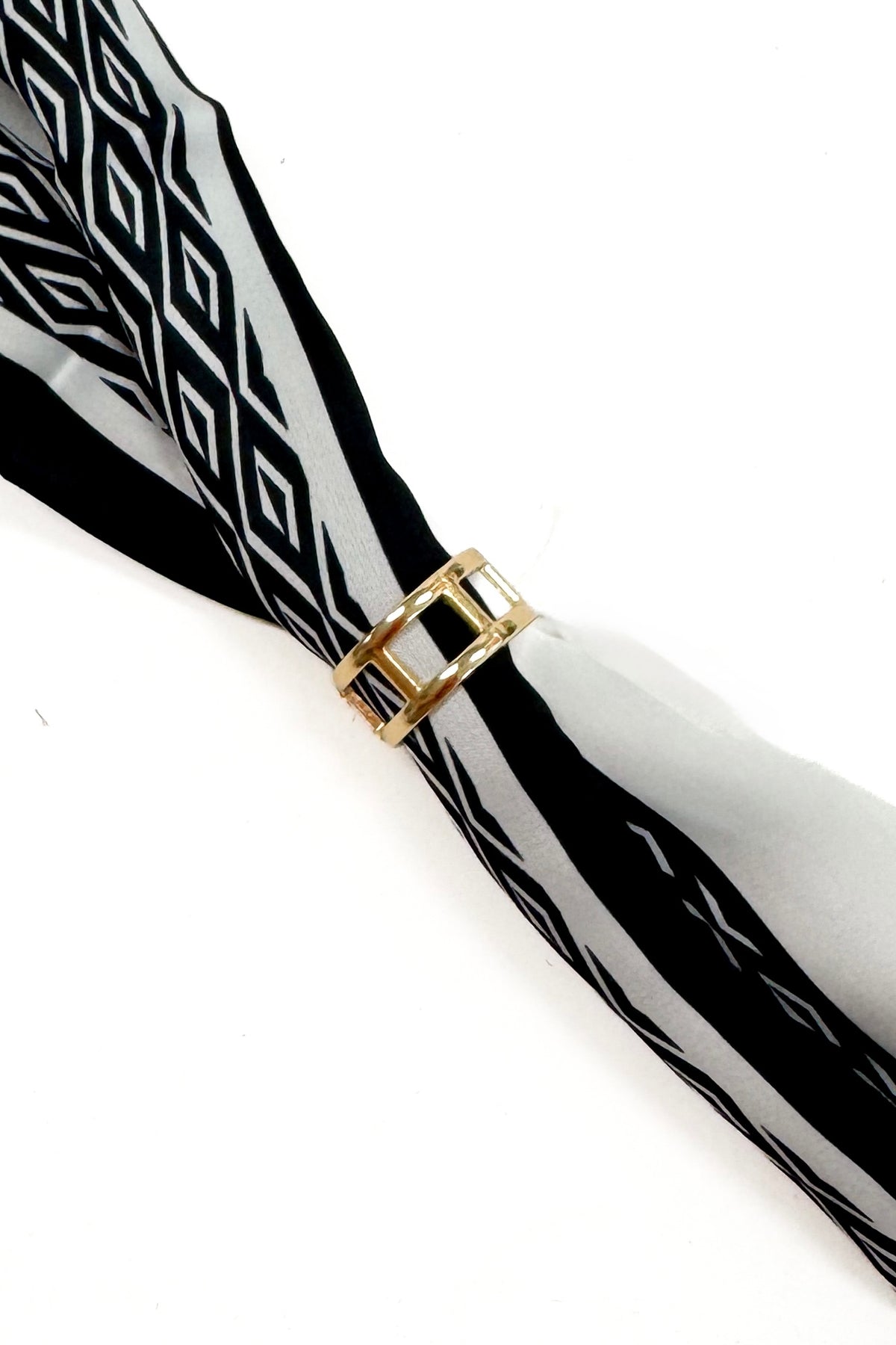 A close-up of a black and white patterned scarf tied with a gold metal ring at the center, set against a plain white background.