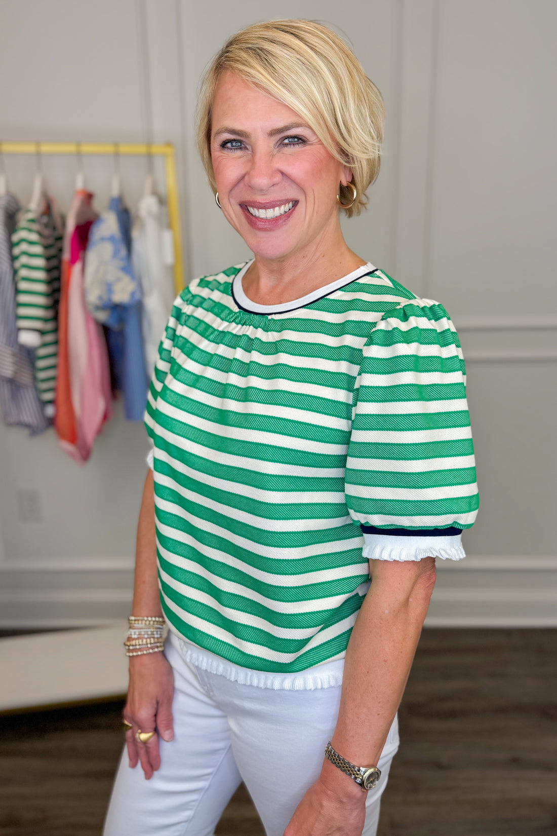 Woman wearing a green and white striped shirt in a room with clothes on hangers.