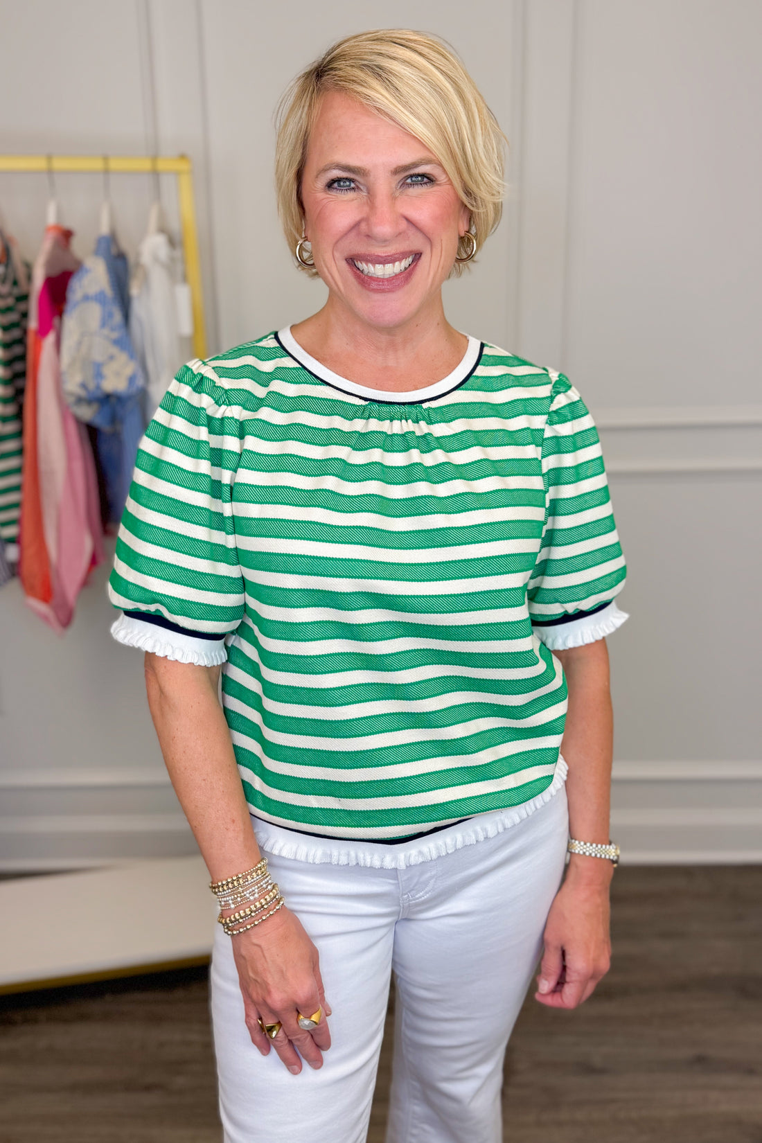 Woman wearing a green and white striped shirt with white pants in a room with clothing racks.