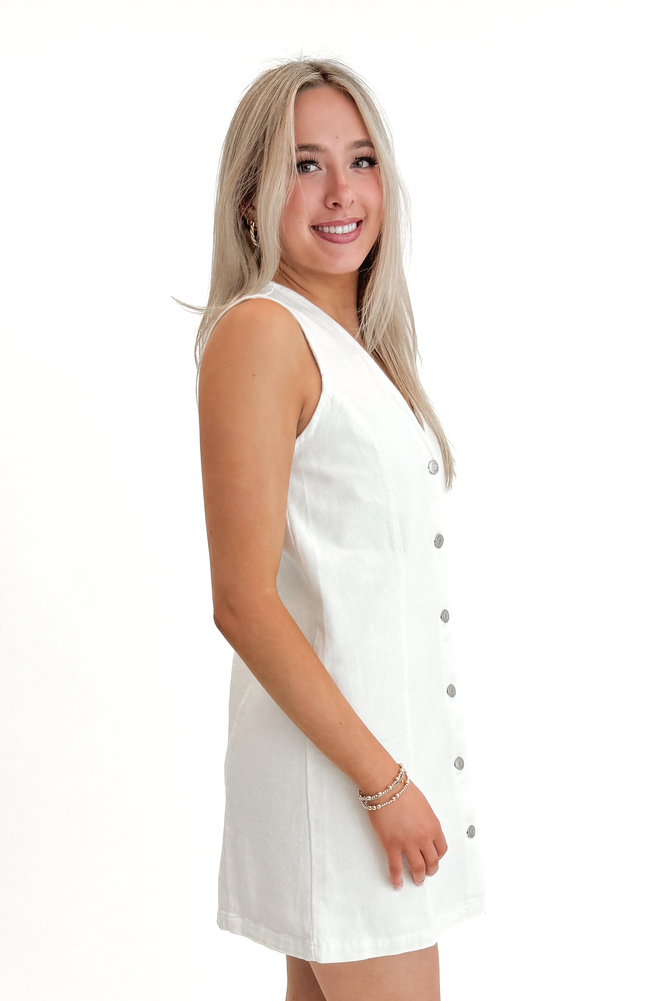 Side view of woman wearing White Denim Button Up Dress against white studio background.