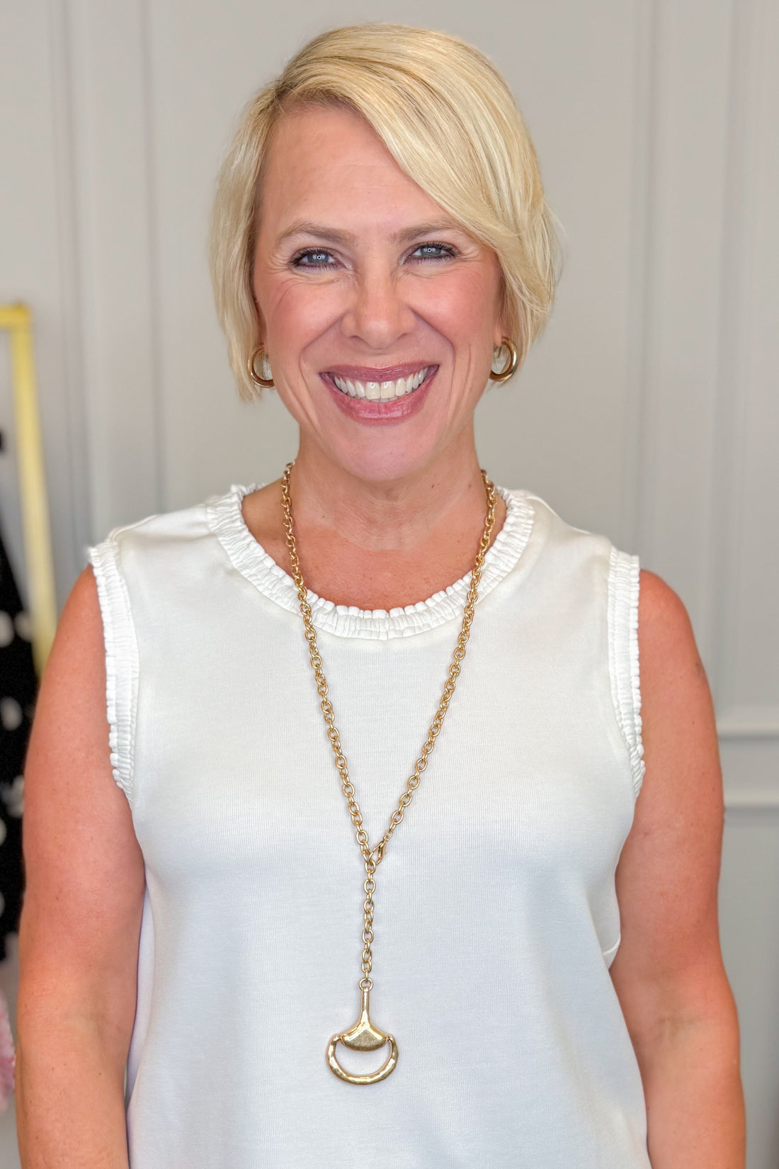 Woman wearing a white sleeveless top and a long necklace with a horesbit pendant.