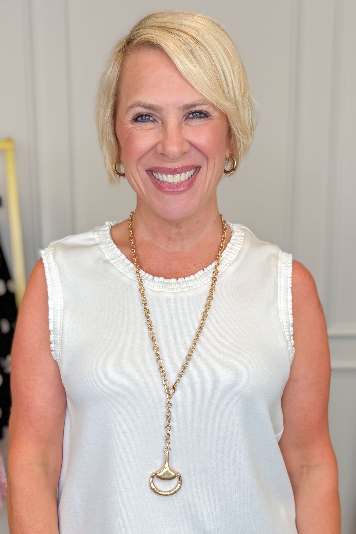 Woman wearing a white sleeveless top and a long necklace with a horesbit pendant.