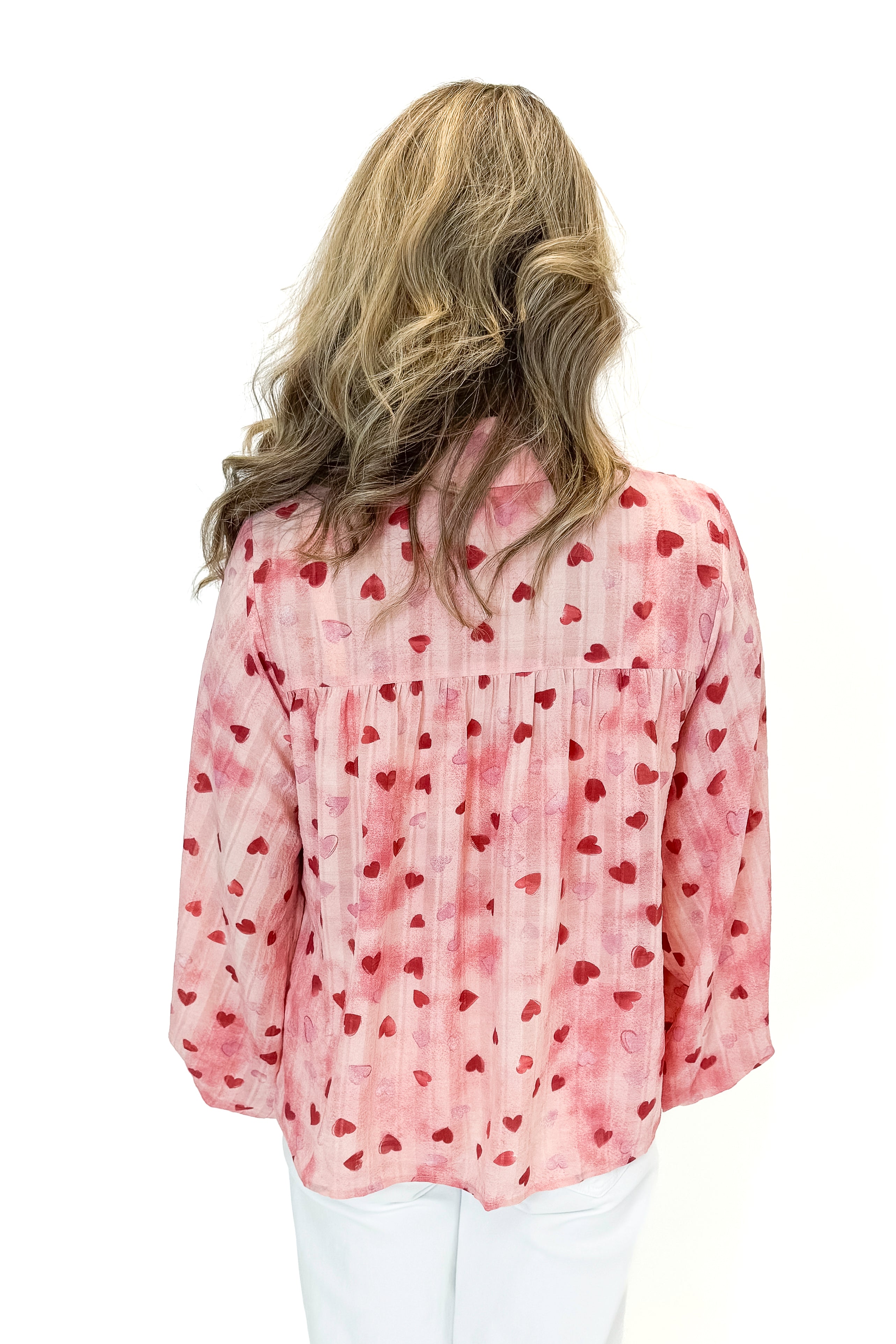 Back view of woman wearing Pink Heart Printed Smocked Detail Top with jeans against white studio background.