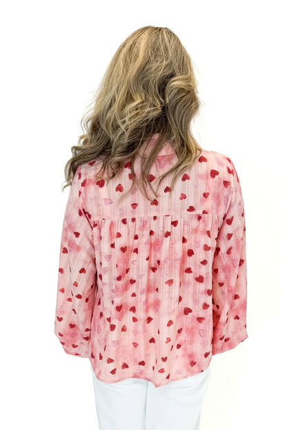 Back view of woman wearing Pink Heart Printed Smocked Detail Top with jeans against white studio background.