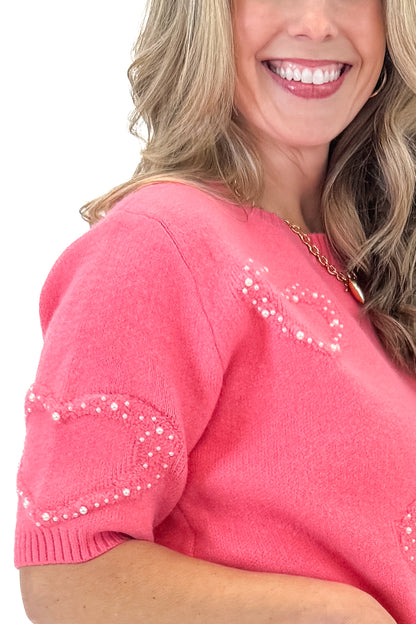 SIde detail view of woman wearing Pink With Pearl Heart Detail Sweater with jeans against white studio background. 